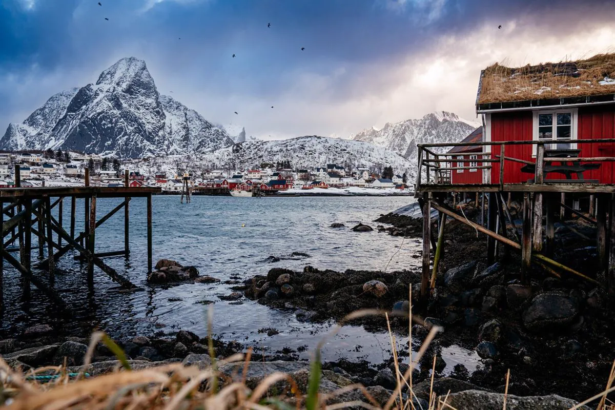 Rote Rorbuer am Wasser, dahinter verschneite Berge