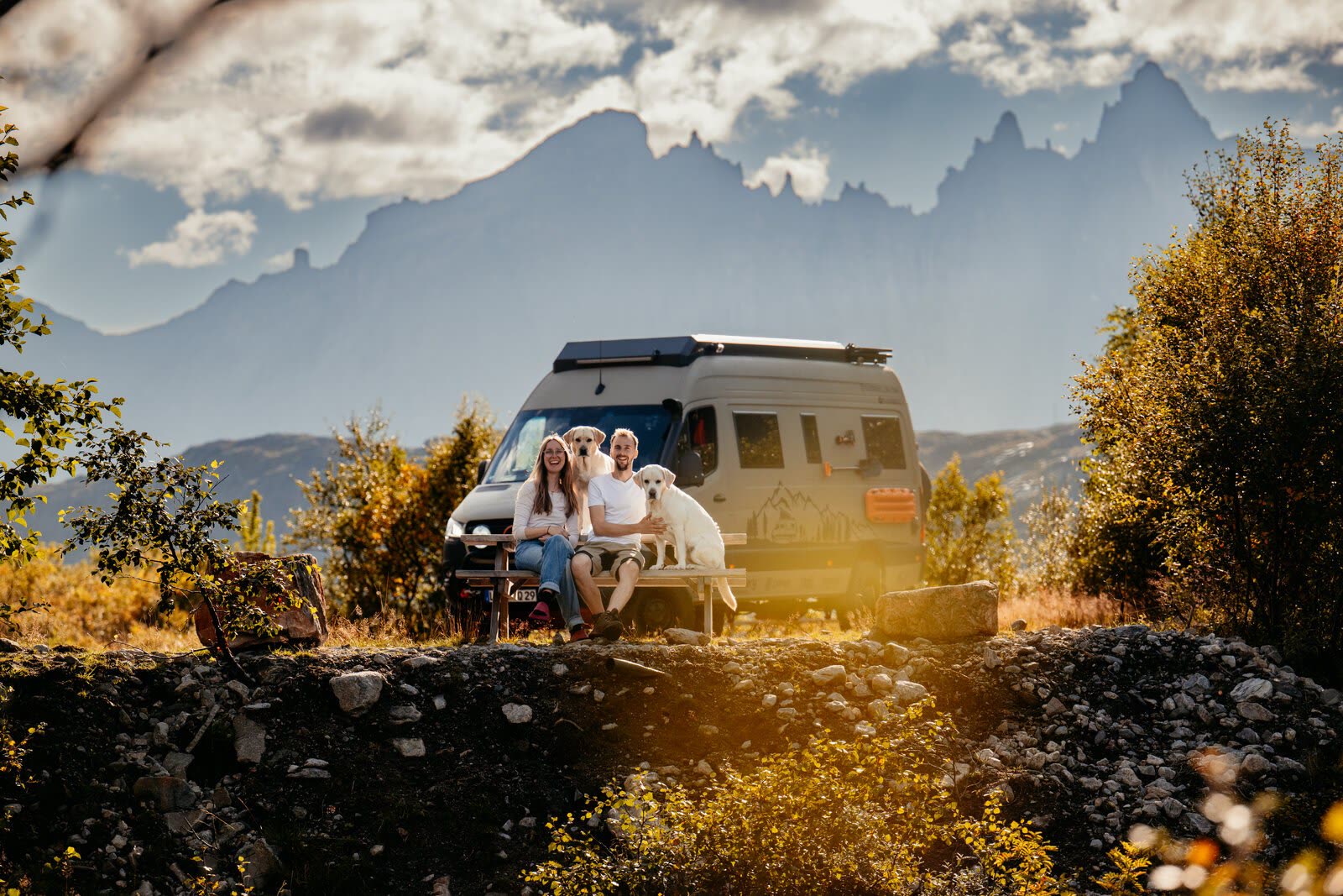 Tomke und Jakob mit Ivy und Alice auf einer Bank vor dem Sprinter, dahinter Berge